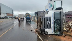 Motorista de caminhão fica ferido após perder controle da direção, bater em muro de casa e tombar