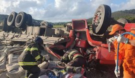 Caminhão com carga de cimento tomba e motorista fica preso às ferragens