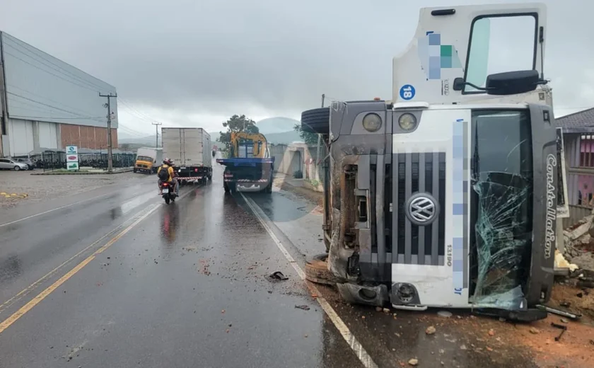 Motorista de caminhão fica ferido após perder controle da direção, bater em muro de casa e tombar