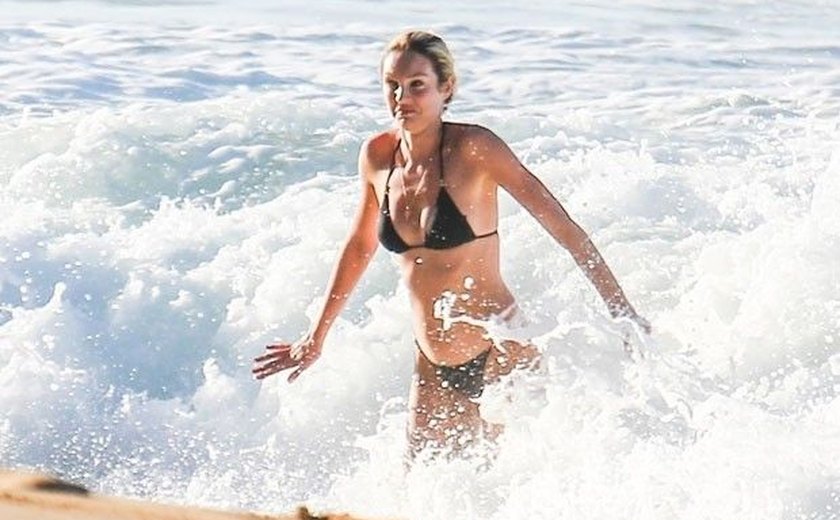 Candice Swanepoel brinca em praia brasileira em visita à família do marido
